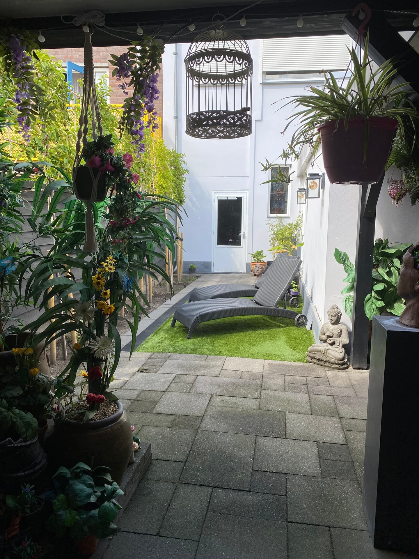 De tuin nu: blauweregen, hangplanten en zicht op het gras met ligbedden