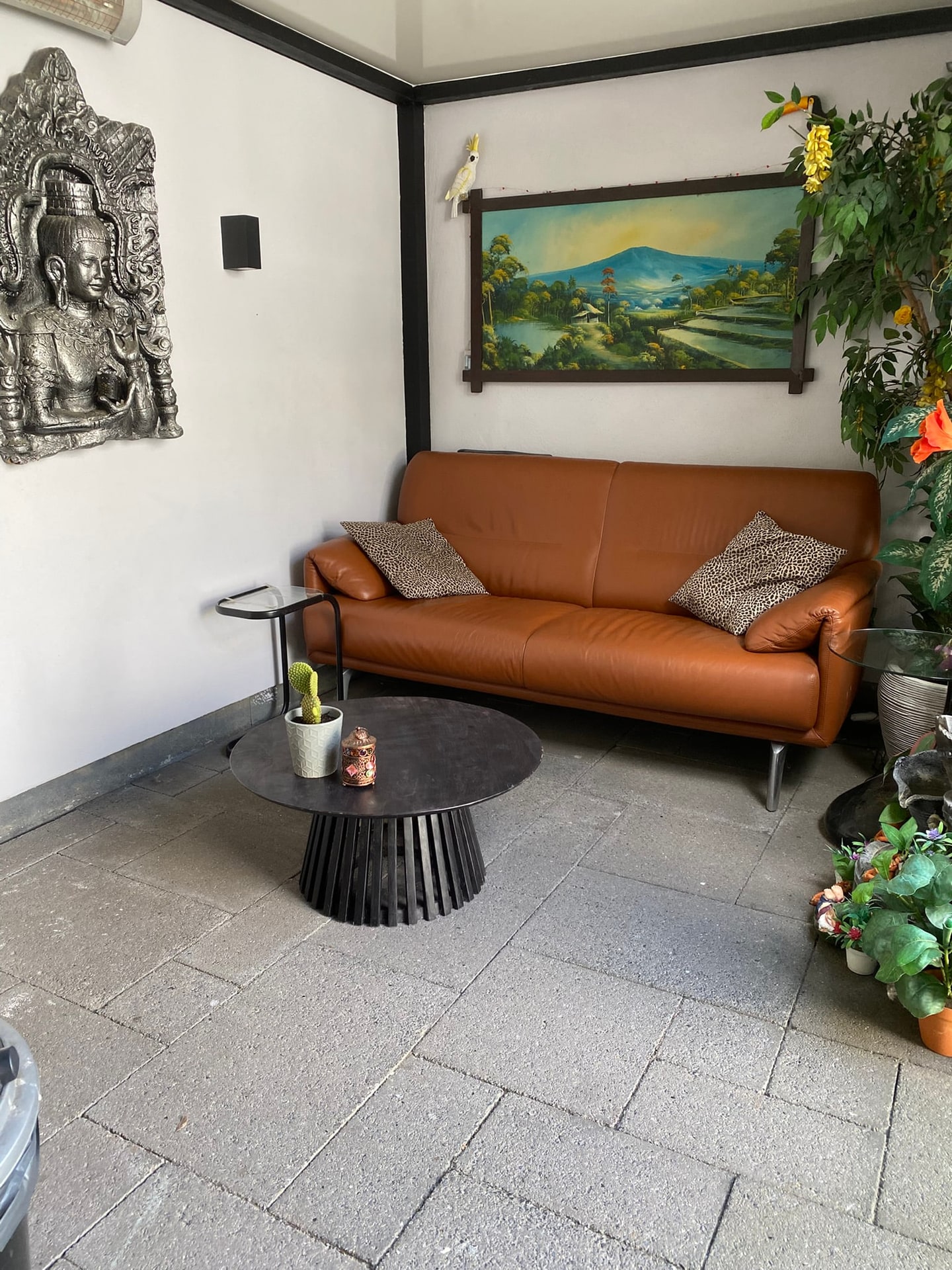 De zithoek onder de overkapping met een leren bank en een schilderij