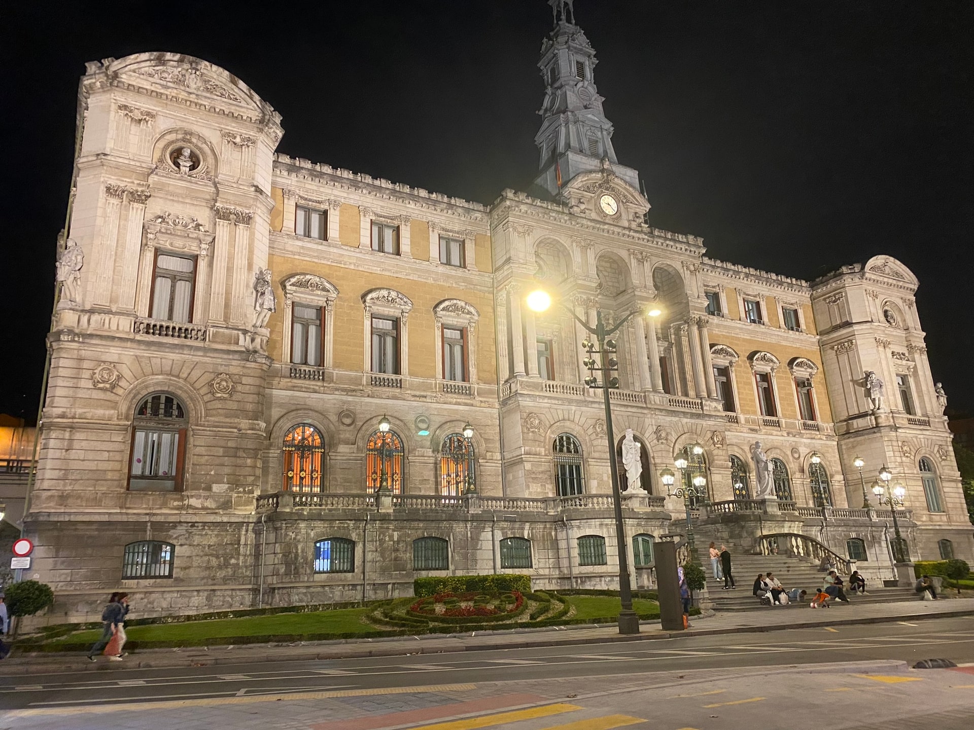 Een rijk versierd historisch stadhuis dat ’s avonds is uitgelicht, met een klokkentoren en beelden tegen een zwarte lucht