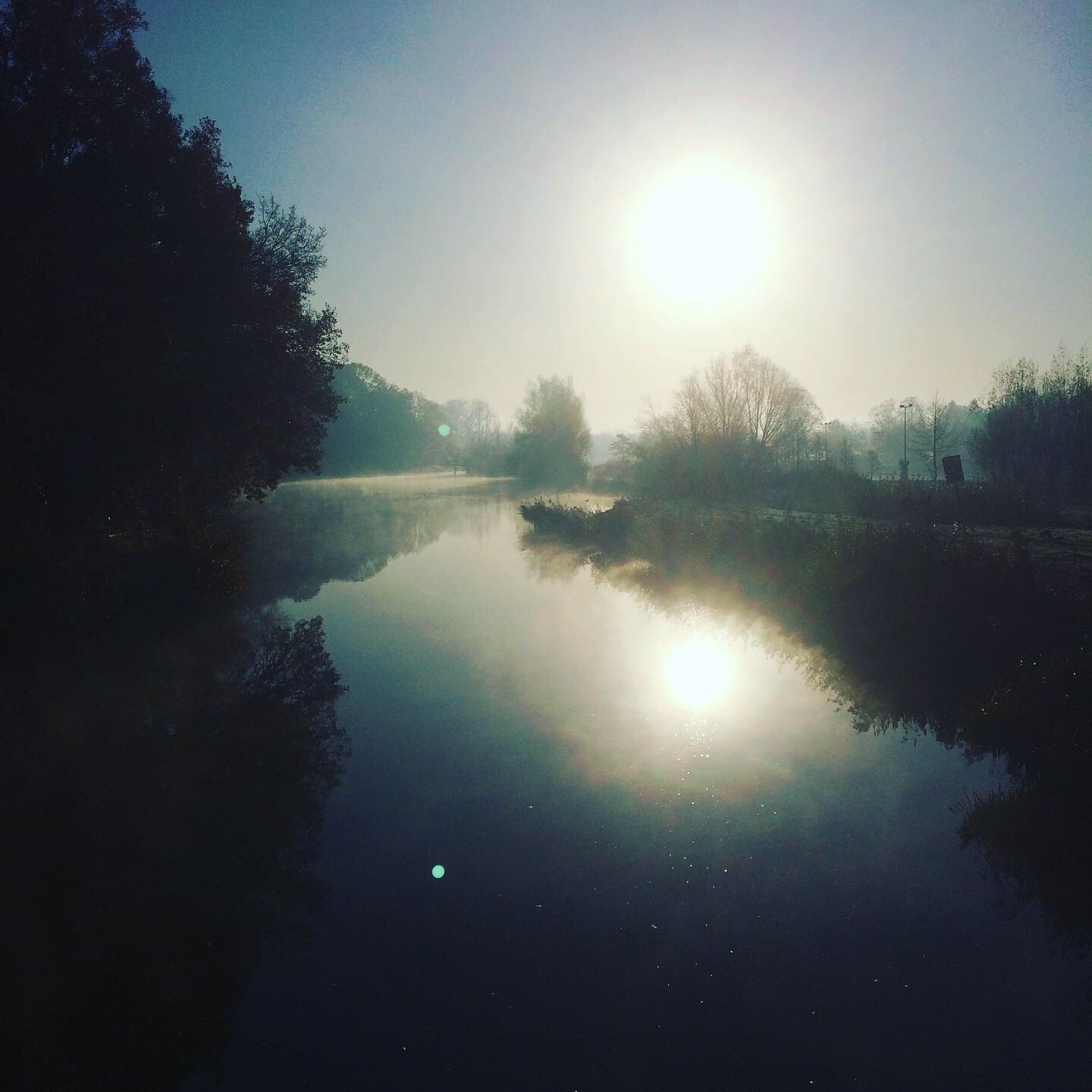 Een rivier bij zonsopkomst, met de zon weerspiegeld in het stille water