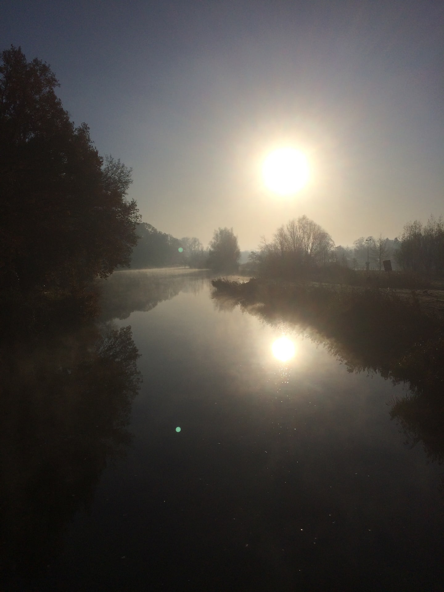 De zon in de mist boven stil water, met de weerspiegeling eronder