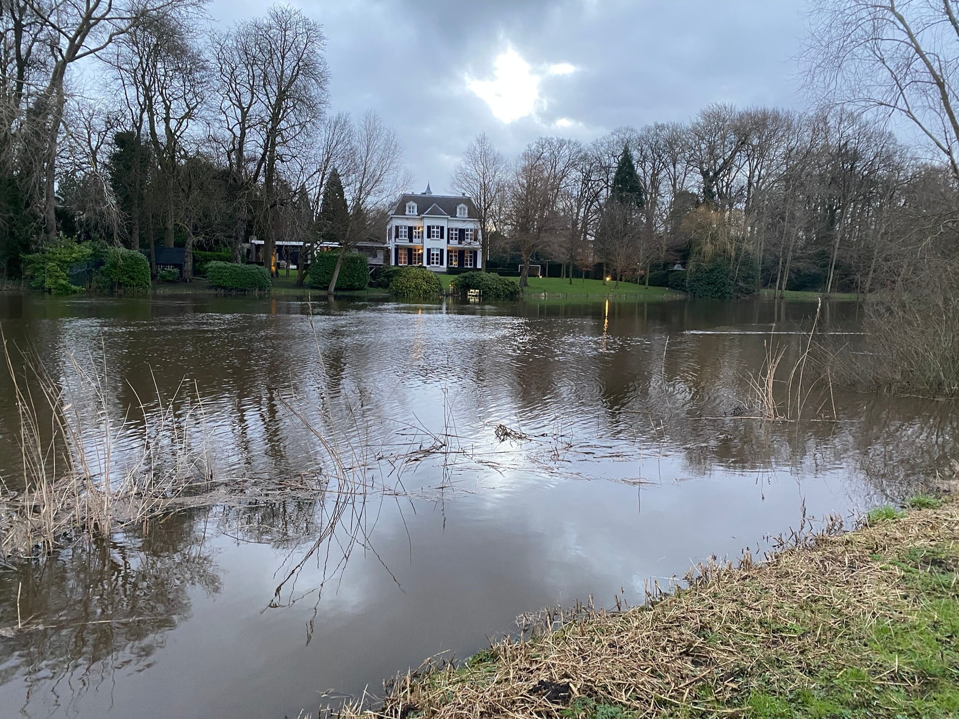Een ondergelopen weiland met een landhuis aan de rand