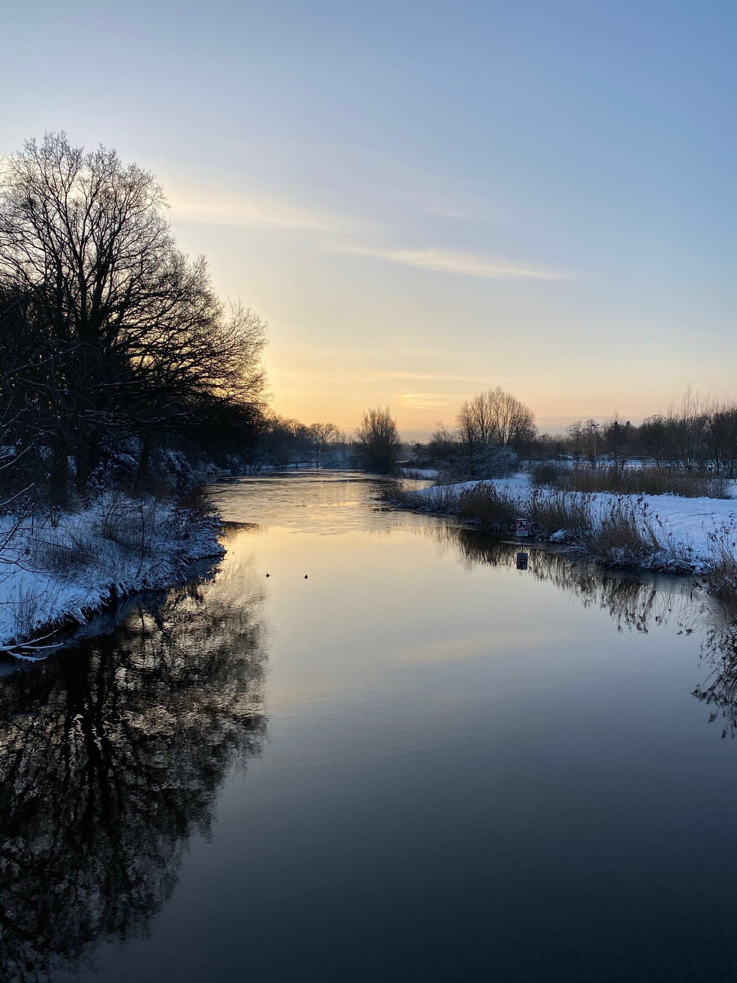 Een rivier in de winter, met sneeuw op de oevers en een bleke lucht erboven