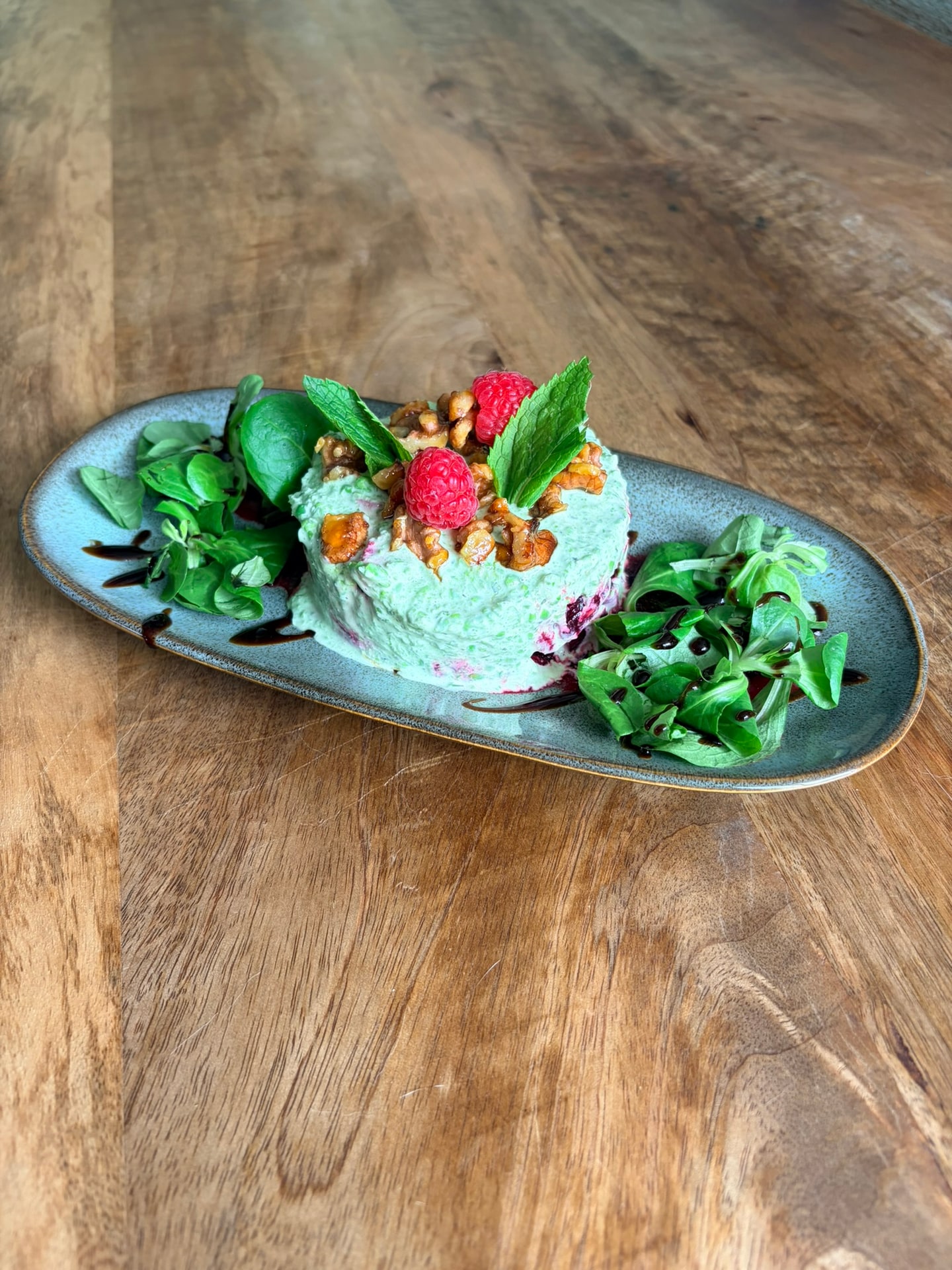 Een torentje groene roomsalade met frambozen, gekarameliseerde walnoten en munt op een ovaal bord