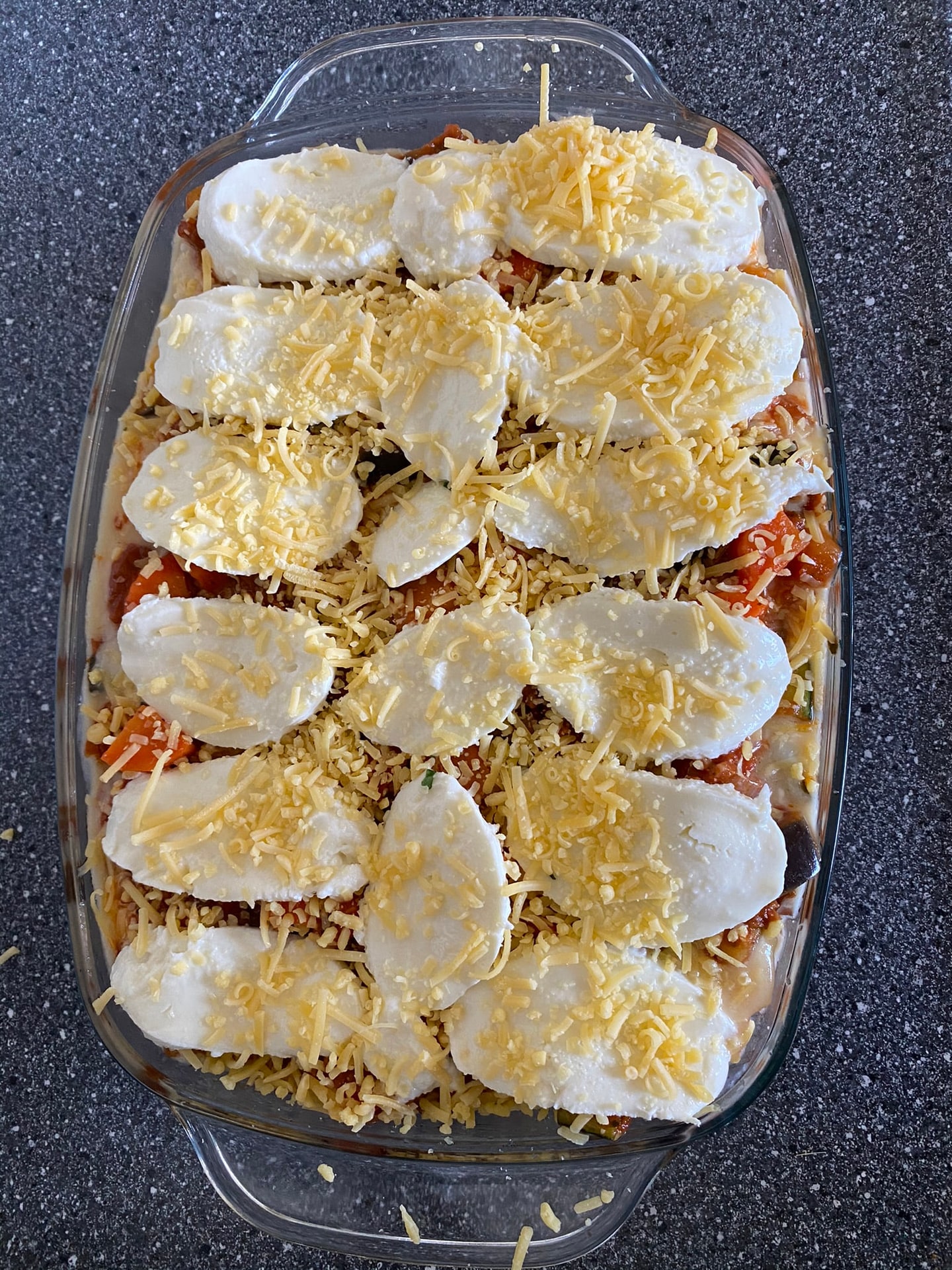 De lasagne voor het bakken, met plakken mozzarella en geraspte kaas erop