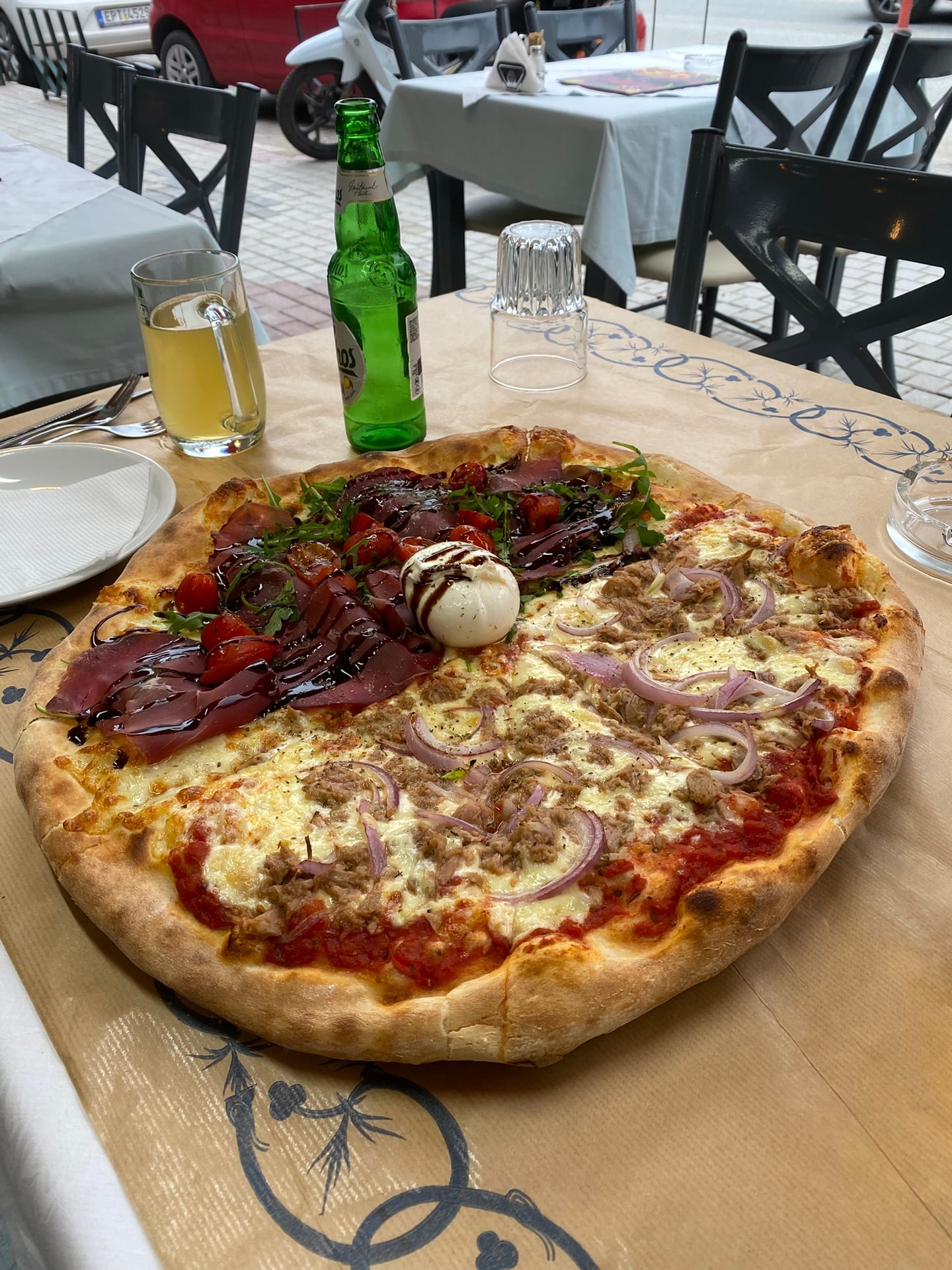 Een pizza met een dikke luchtige rand, half belegd met rauwe ham en rucola