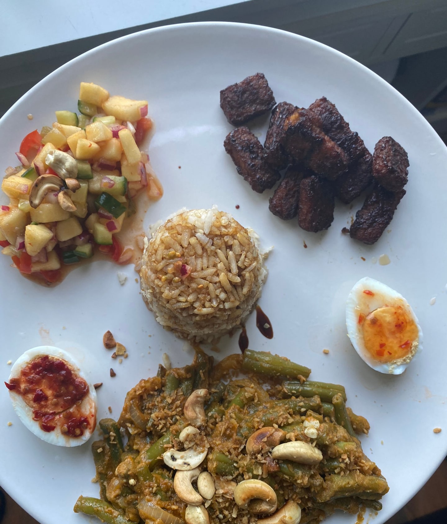 Een bord met fruitsalsa, rijst, gekruid vlees, ei en sperziebonen met cashews