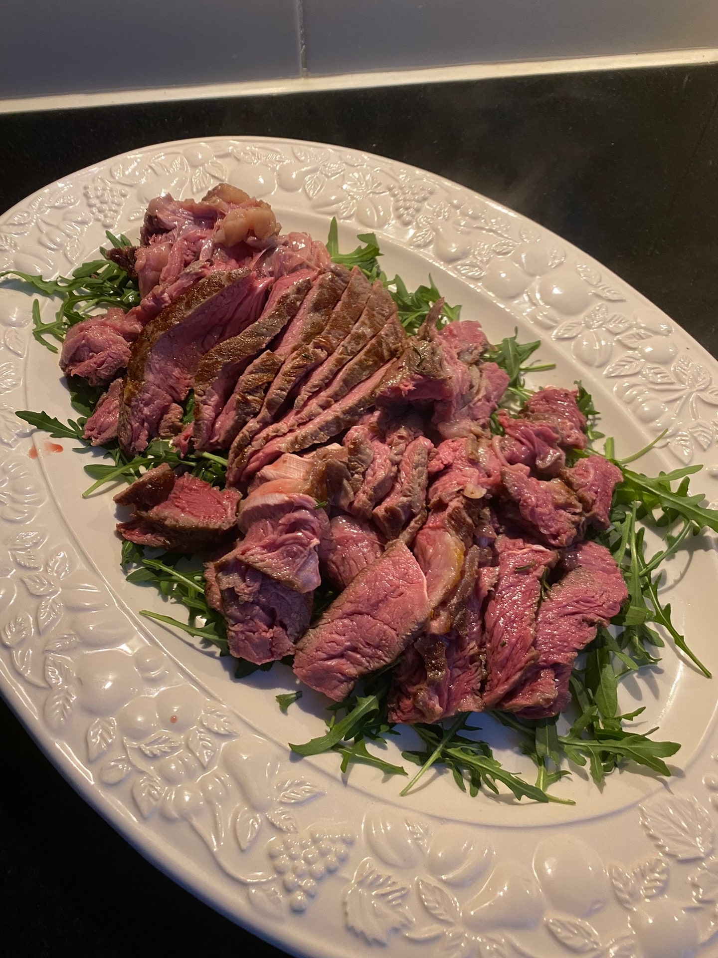 Plakken rosé gebakken rundvlees op rucola, op een witte schaal