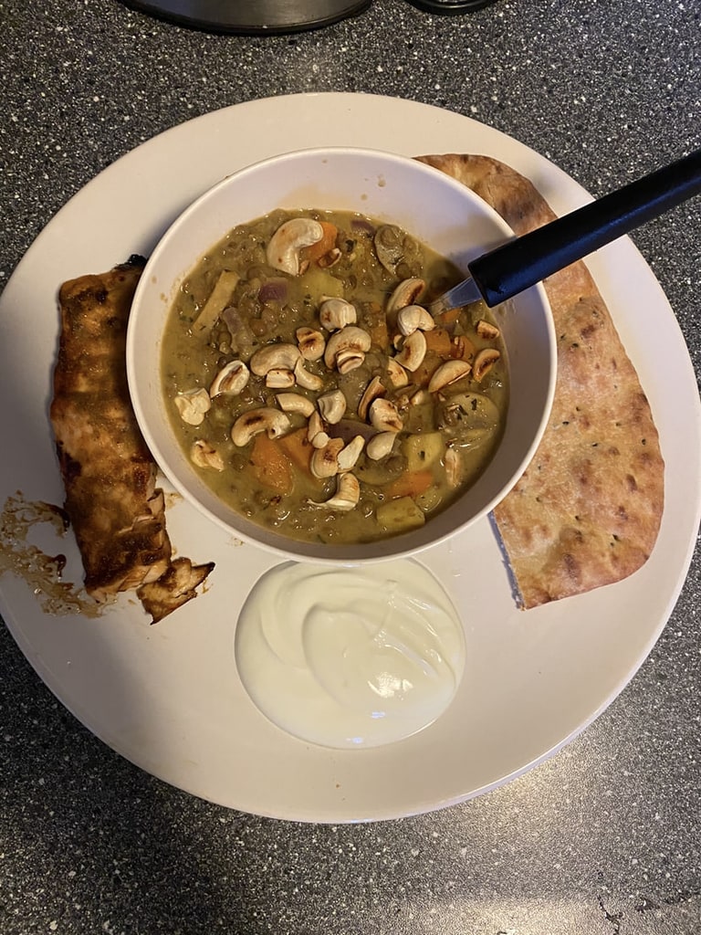 Een kom kerrie met naanbrood en yoghurt ernaast
