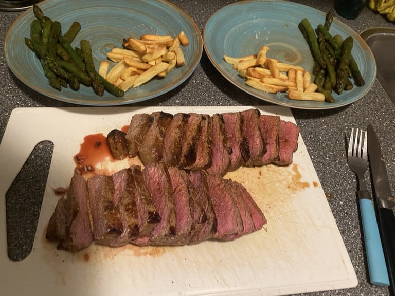 Plakken gebakken biefstuk op een snijplank, met asperges