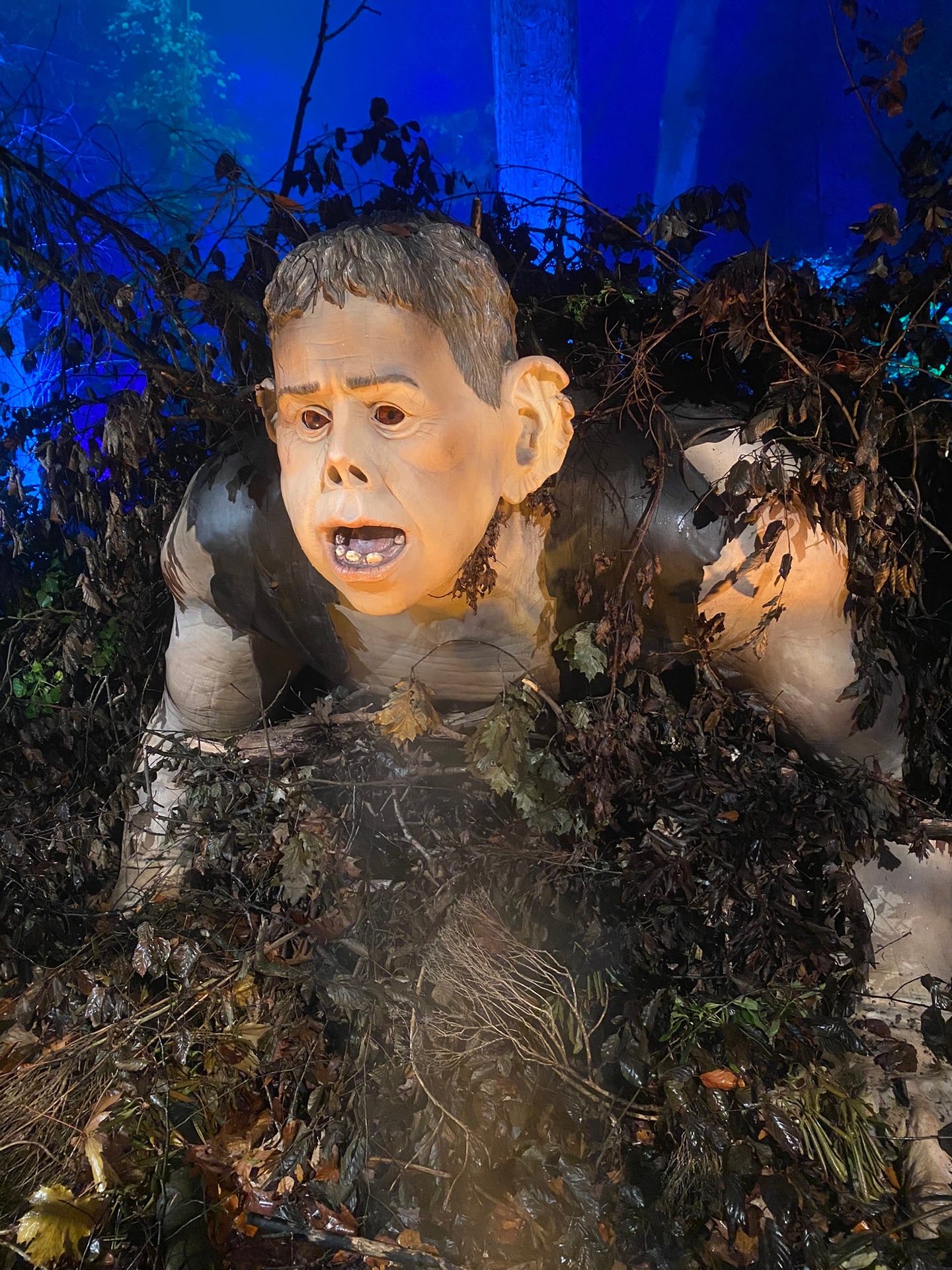 Een reuzenfiguur die hoog tussen de bomen uit komt, aangelicht in het donker