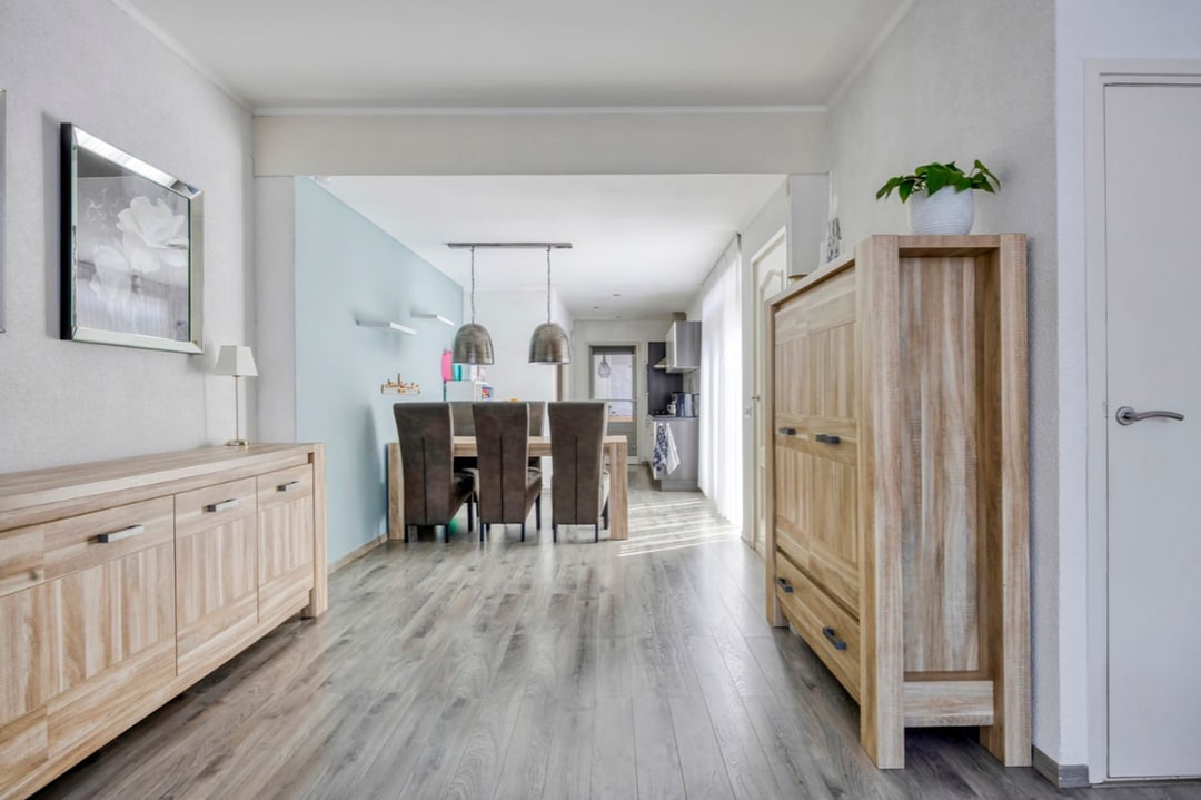 De huiskamer op de verkoopfoto: witte en lichtblauwe wanden, licht houten meubels