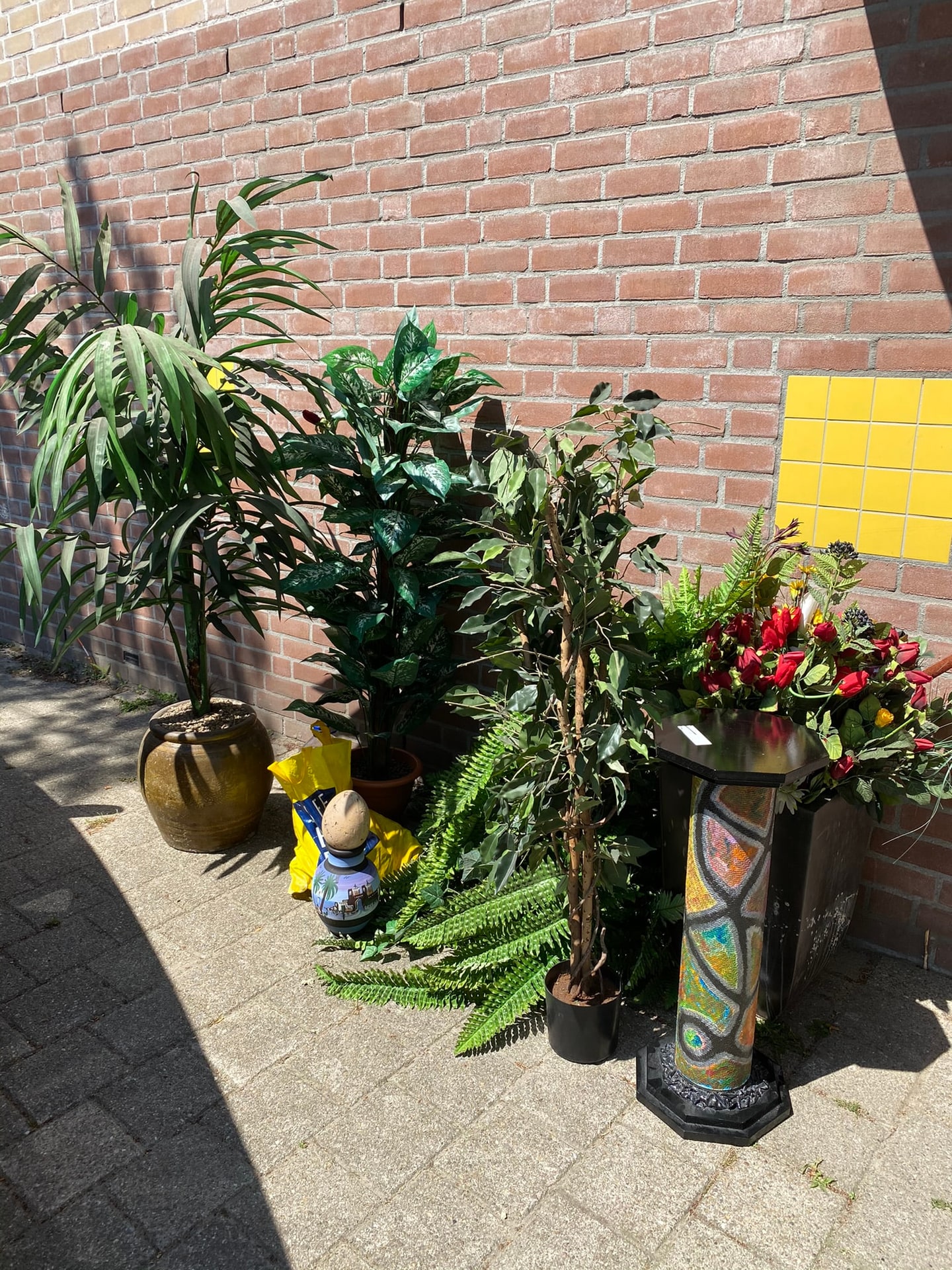 Planten, potten, varens en een kabouter bij elkaar tegen een bakstenen muur, thuis uitgestald