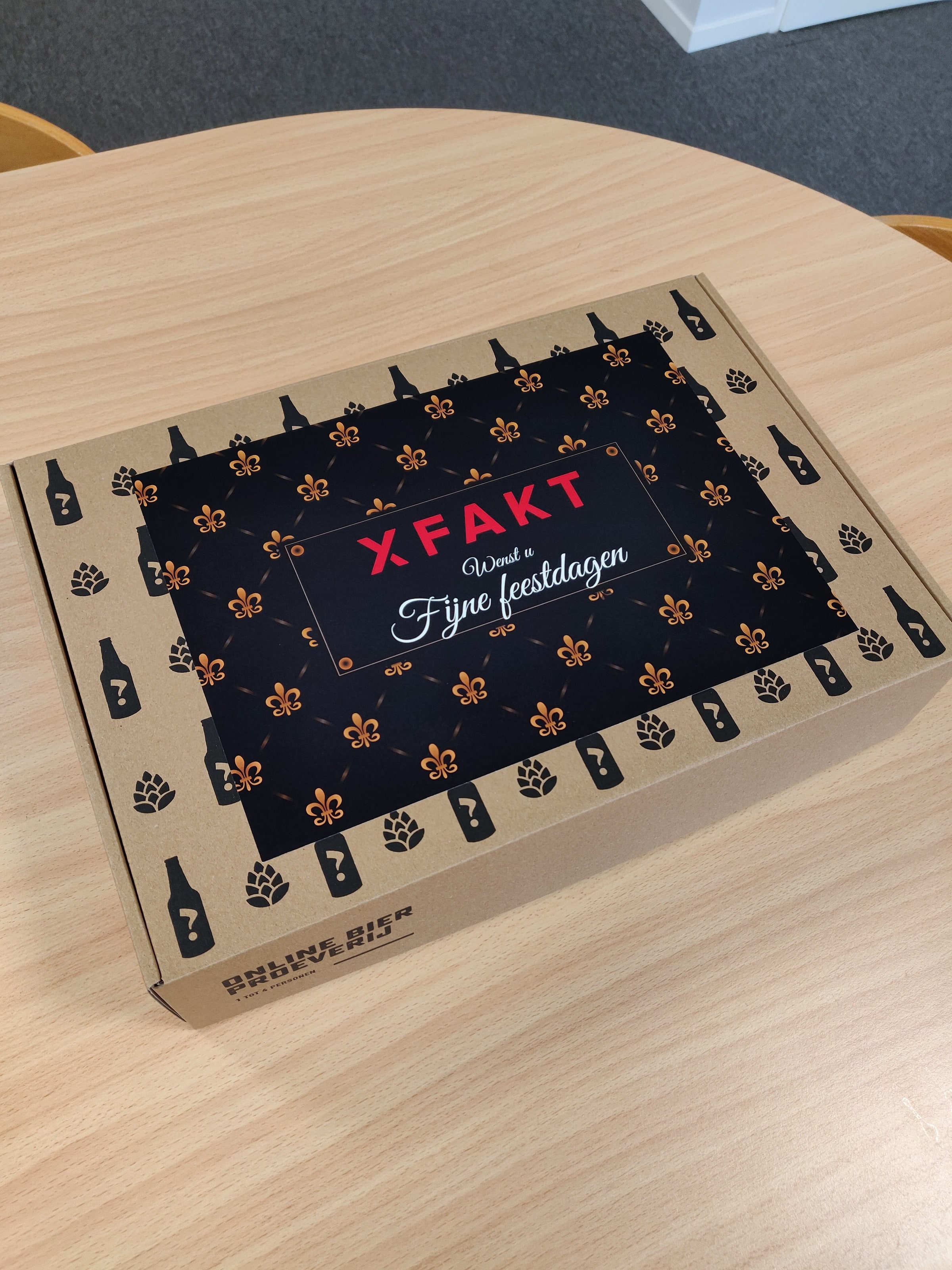 De gesloten doos op een tafel, met een patroon van flesjes en hoppebellen en een donkere sleeve met een feestdagenwens